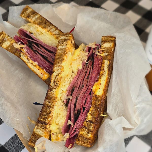 A Main St. Deli Reuben sandwich, cut in half, with pastrami, sauerkraut, and melted cheese.