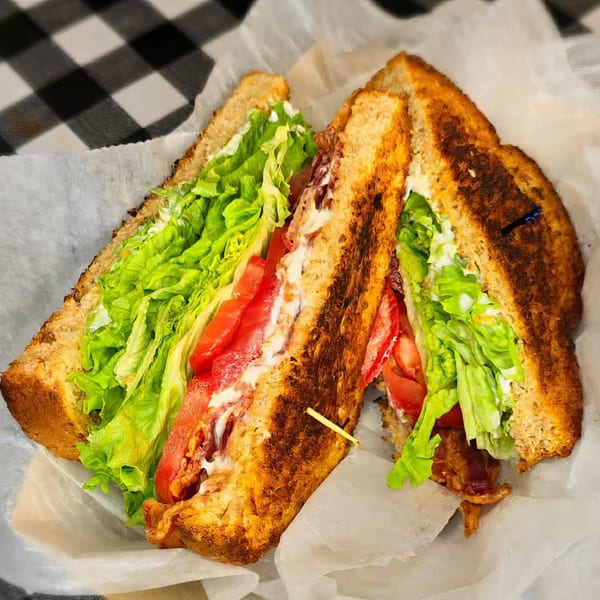 A toasted Main St. Deli BLT sandwich, cut in half, with bacon, lettuce, tomato, and mayonnaise.