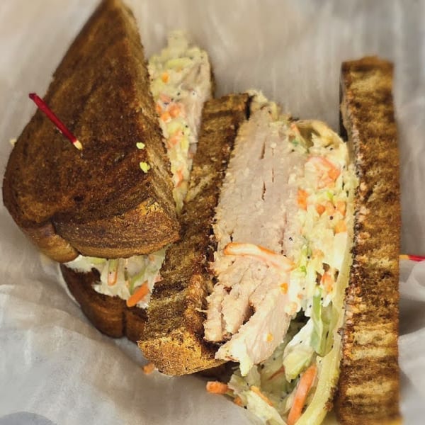 A Main St. Deli sandwich with sliced turkey, coleslaw, and dark toasted bread.