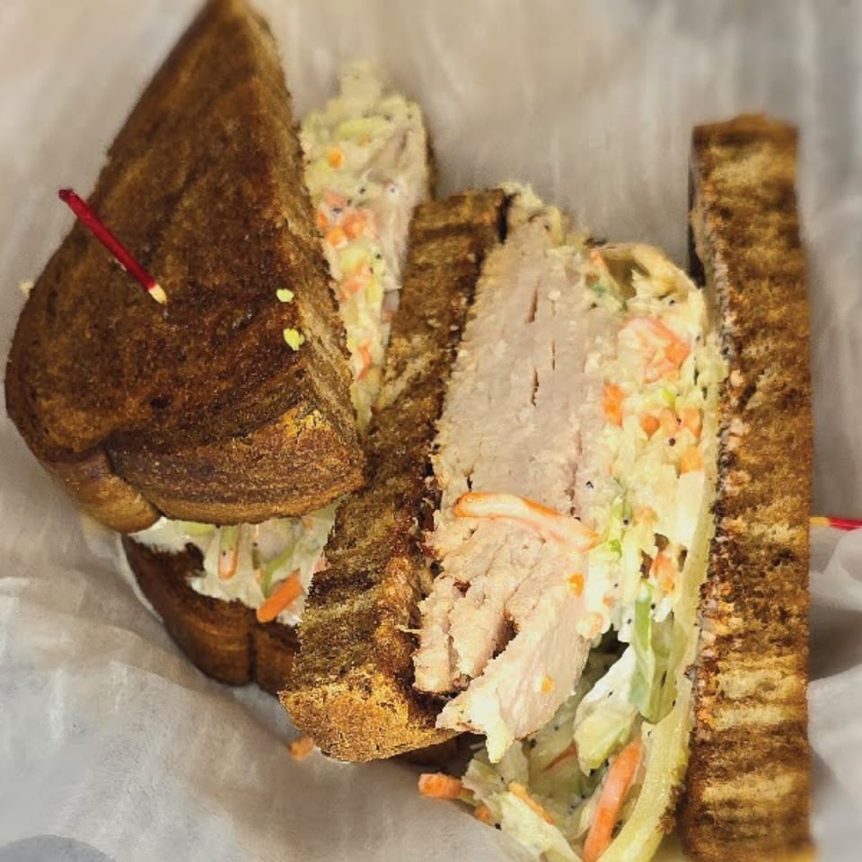 A Main St. Deli sandwich with sliced turkey, coleslaw, and dark toasted bread.
