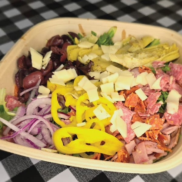 A deli salad with olives, artichoke hearts, cheese, meats, peppers, and red onions in a bowl.