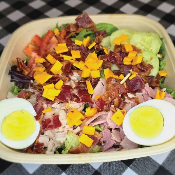 A deli salad with lettuce, tomatoes, cucumbers, bacon, ham, turkey, cheddar cheese, and hard-boiled eggs.