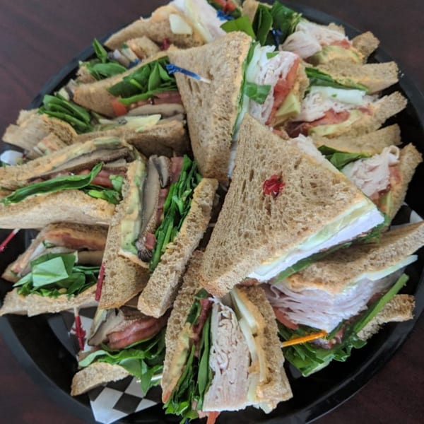 A platter of Main St. Deli sandwiches, cut into triangles, with various fillings like turkey, avocado, and lettuce.