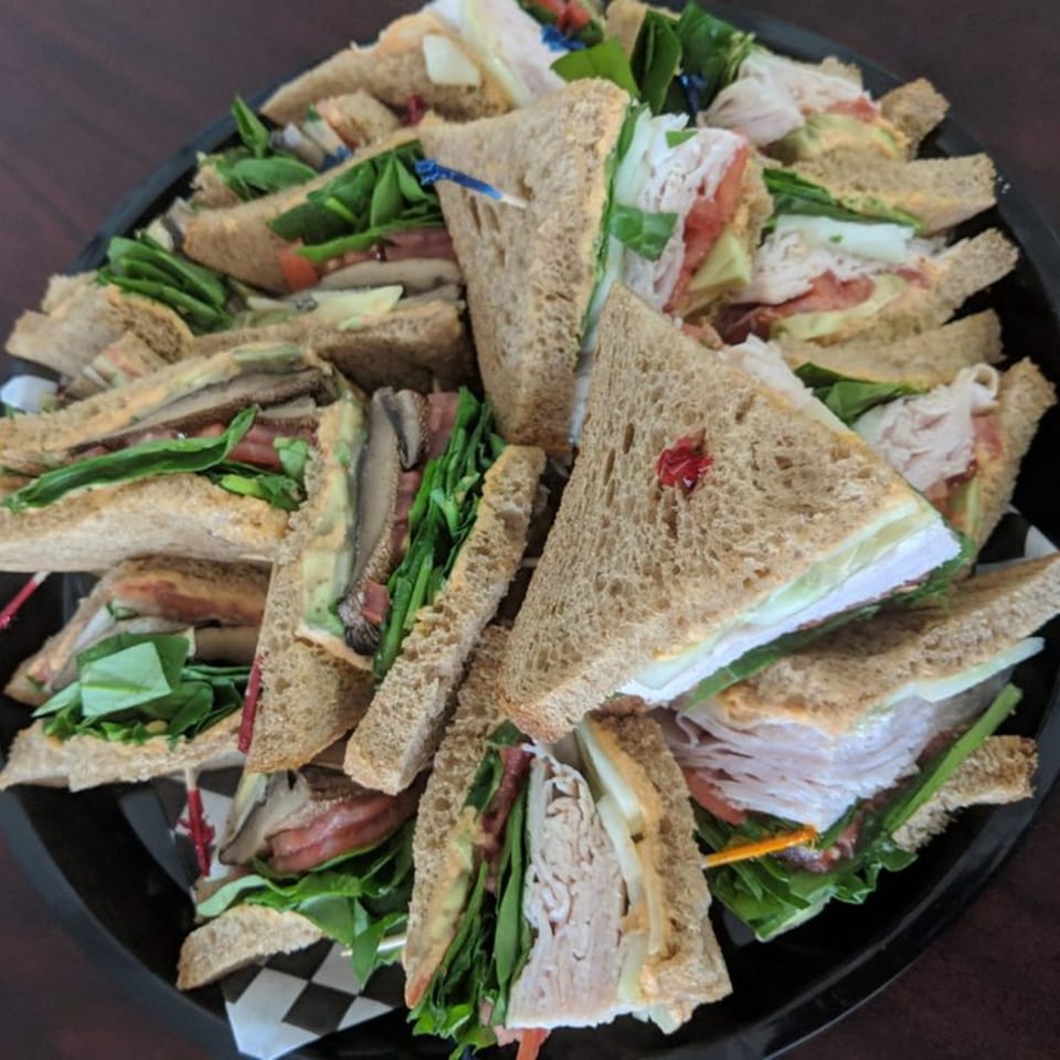 A platter of Main St. Deli sandwiches, cut into triangles, with various fillings like turkey, avocado, and lettuce.