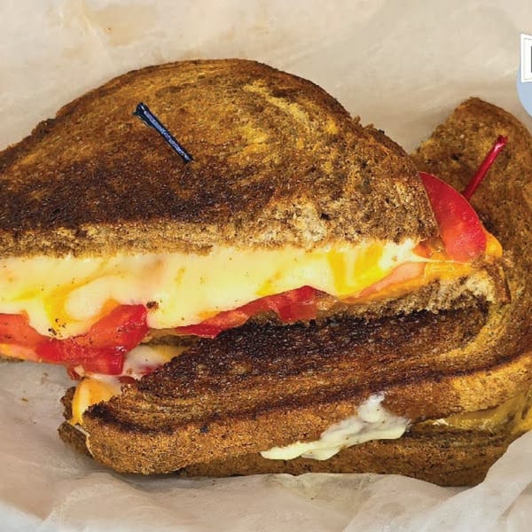 Grilled cheese sandwich with melted cheese and sliced tomatoes, served on toasted rye bread.